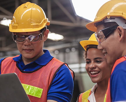three workers in hard hats and safety gear inspect an item