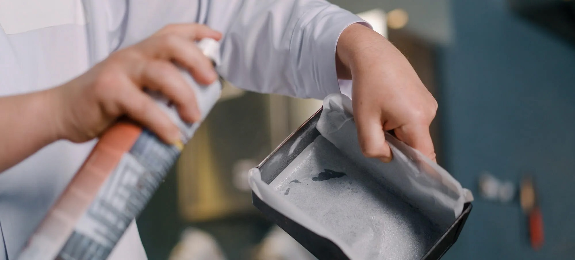 Close up of the arms of a chef spraying a pan with cooking spray.  